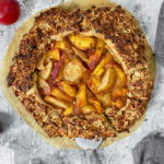 A freshly baked peach almond galette with plums around it.