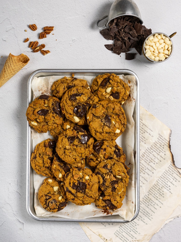 Baking sheet of pumpkin chocolate chip cookies with recipe card and scattered ingredients. 