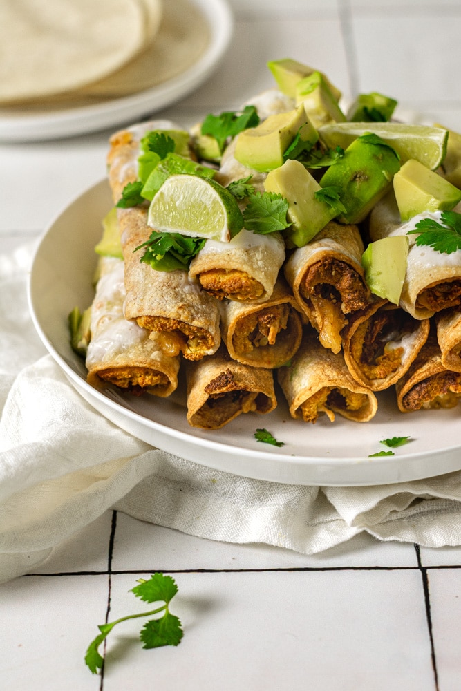 close up shot of taquitos with avocado and cilantro on top