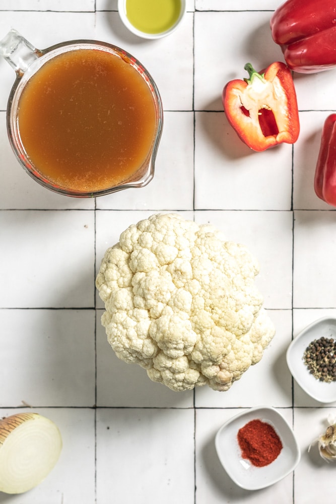 the ingredients to make soup, including red pepper, olive oil, cauliflower, vegetable broth, smoked paprika, thyme, garlic, and onion.