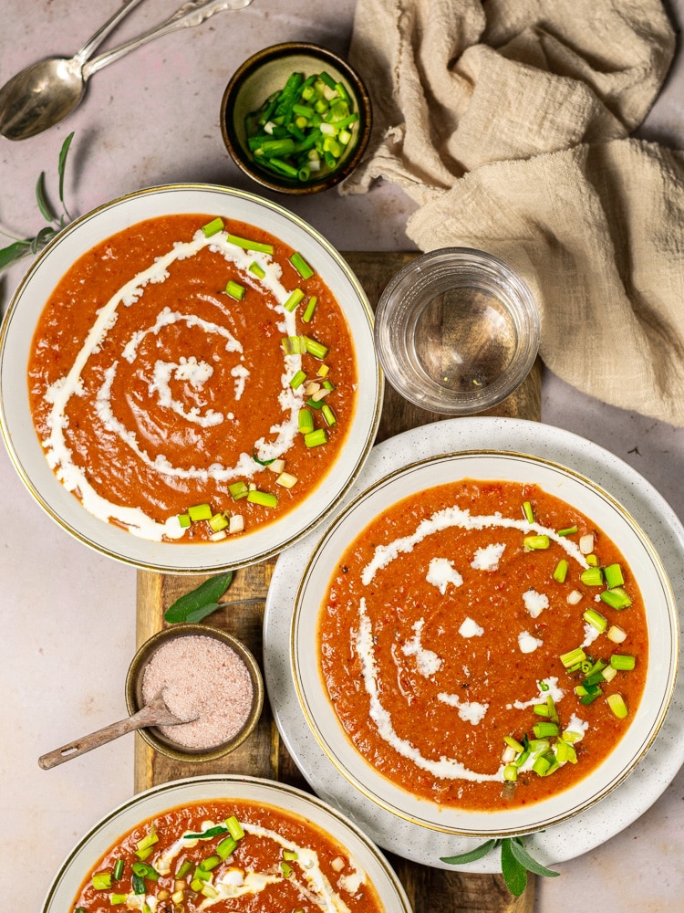 three bowls of soup drizzled with coconut cream and green onions on a table