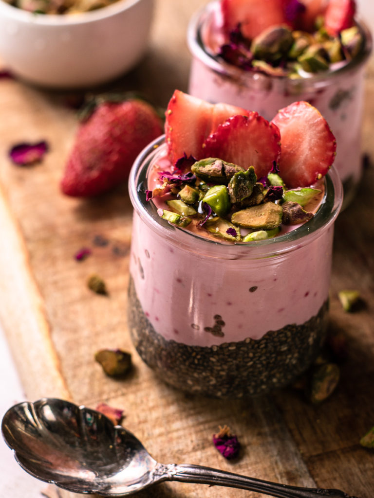 Two jars of chia pudding with fresh strawberries on top and pistachios. 