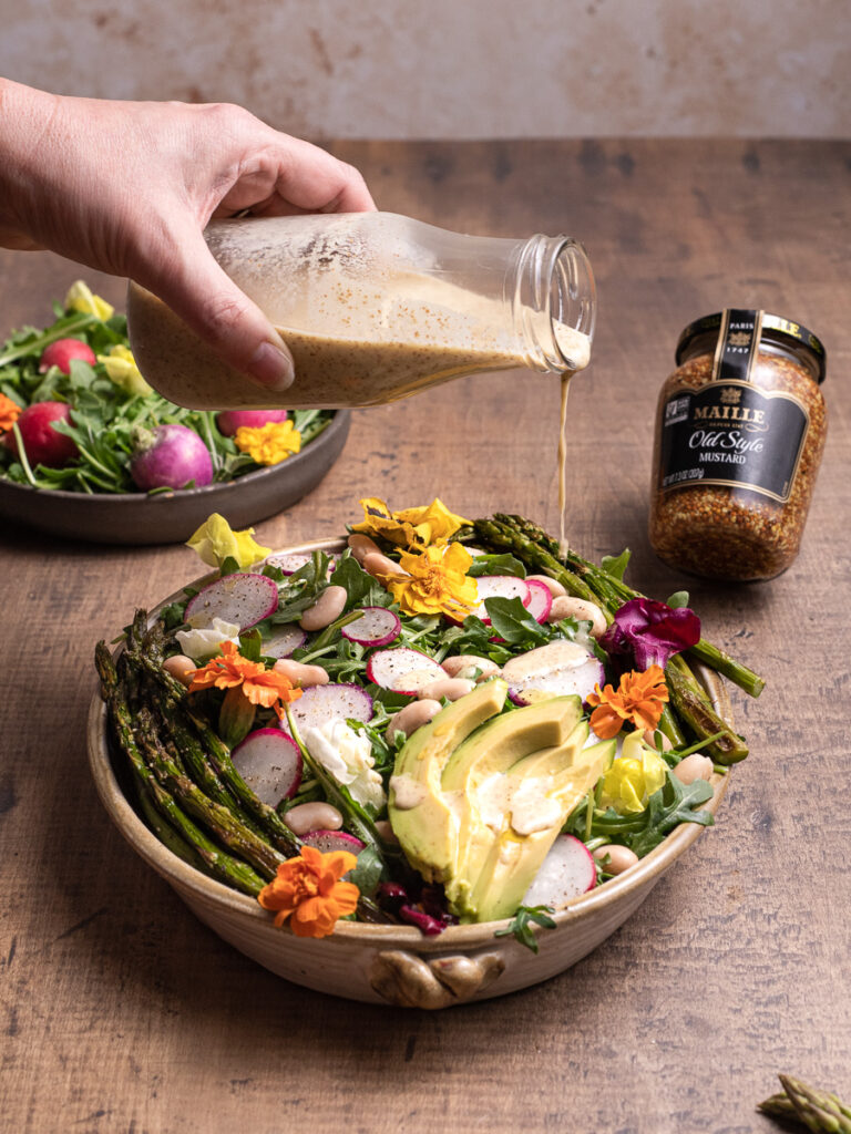 Drizzling creamy mustard dressing over a garden fresh salad. Featuring wild flowers, fresh avacado, and asaparagus. 