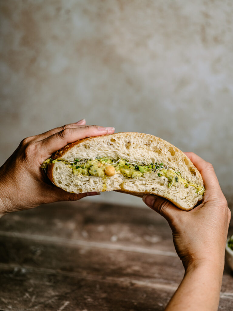 Holding a big vegan sandwich with broccoli sprouts