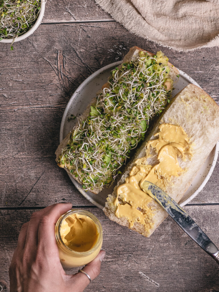 spreading mustard on a chickpea avocado salad sandwich